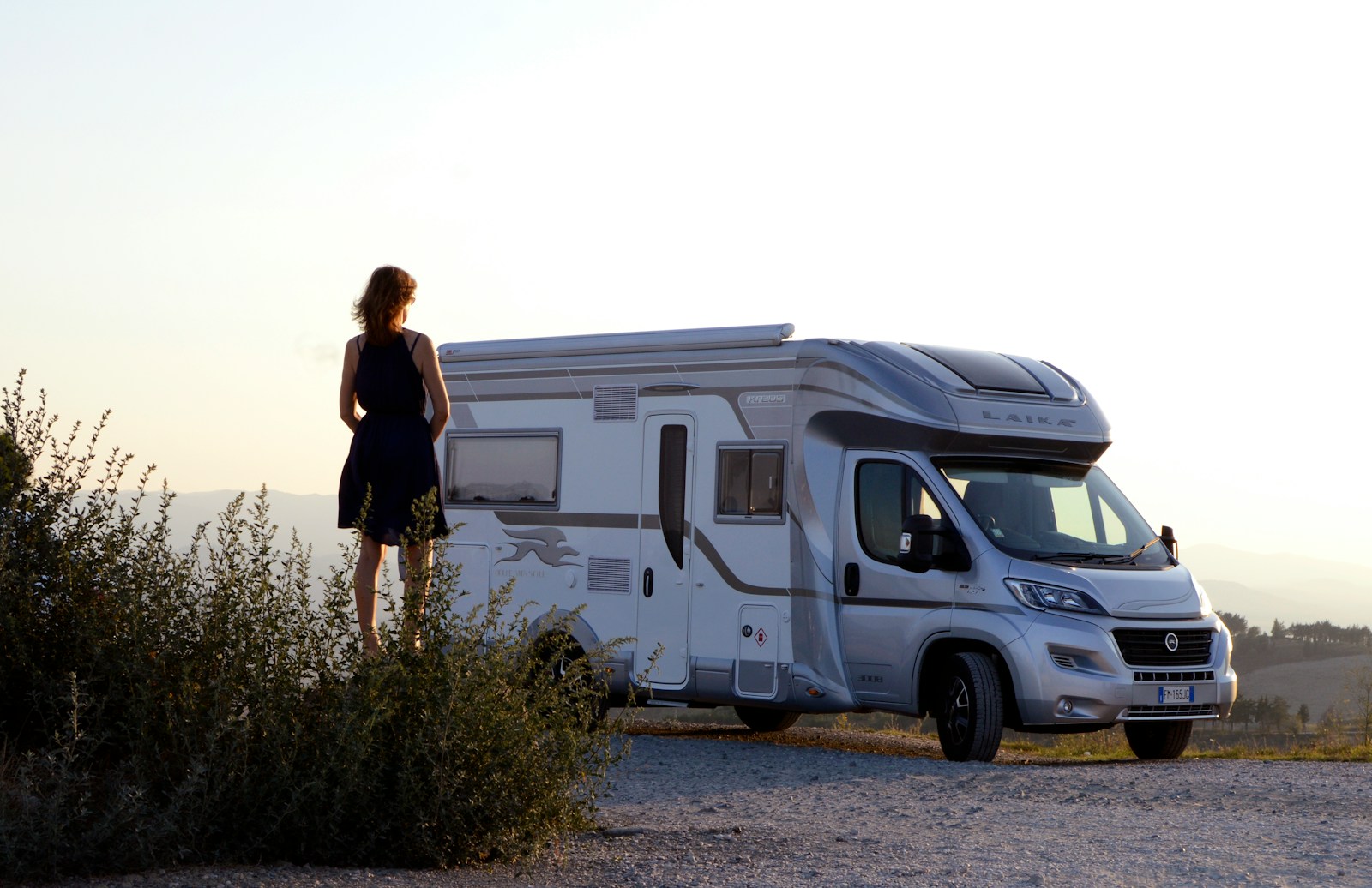 woman in black dress standing beside white and blue rv trailer during daytime